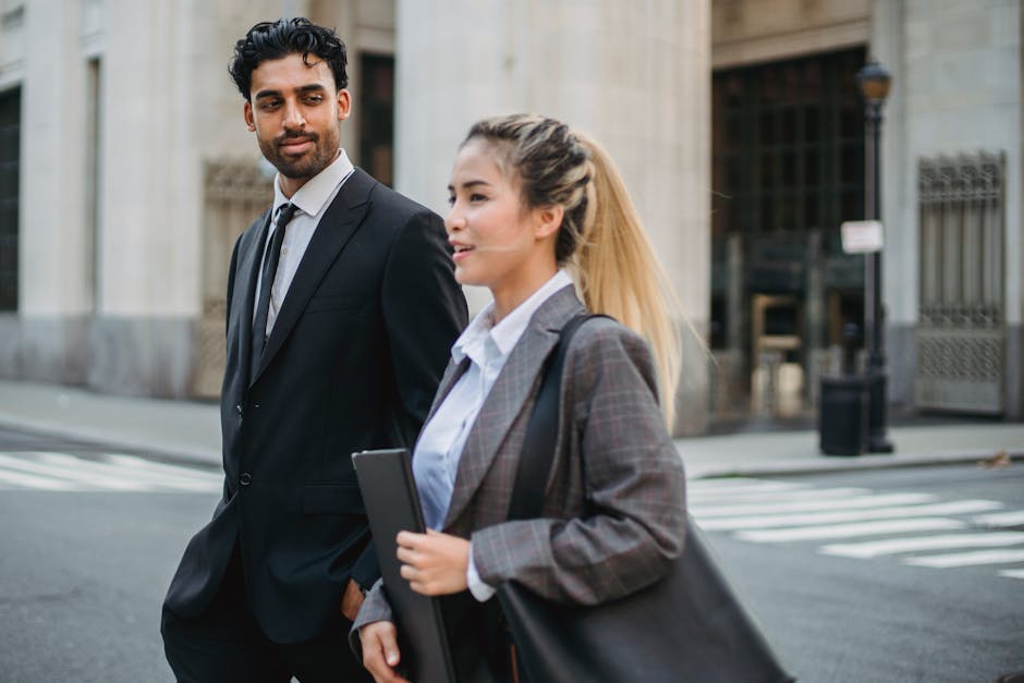 Two business professionals in formal attire walking on a city street, engaged in conversation
