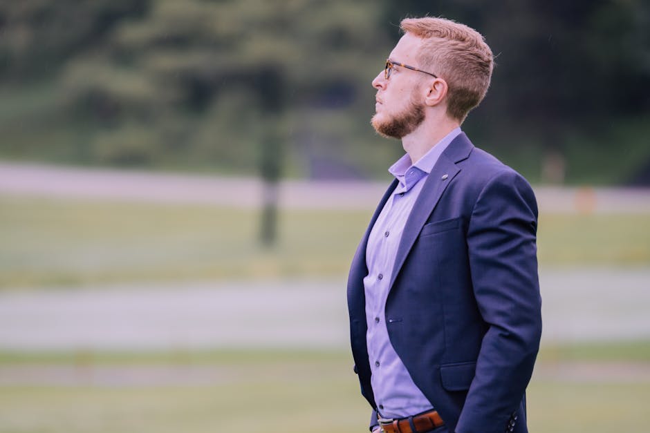 Side profile of a businessman in a suit standing outdoors with a blurred green background
