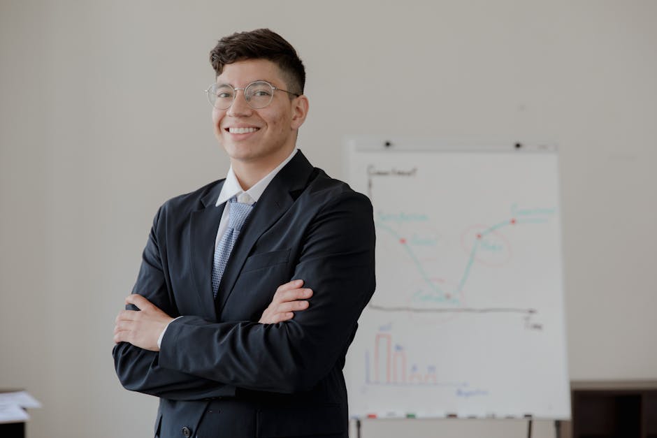 A smiling businessman with crossed arms in a formal suit stands near a whiteboard