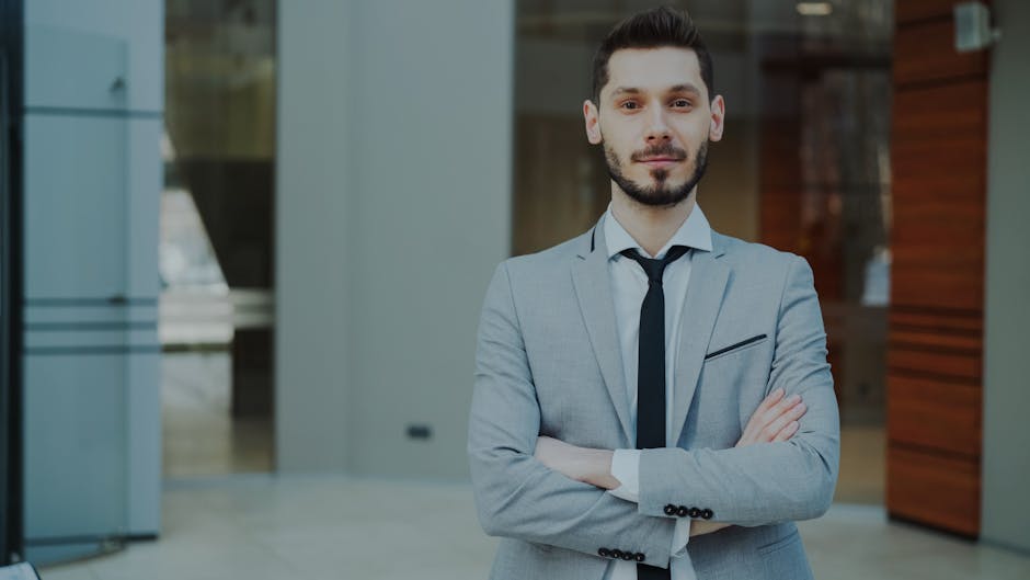 Businessman in a sleek gray suit with arms crossed, looking confident in a modern office